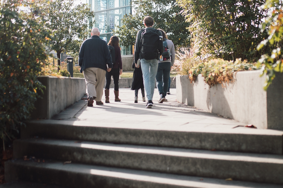 A varied group of people walks away from camera into a slightly hazy distance
