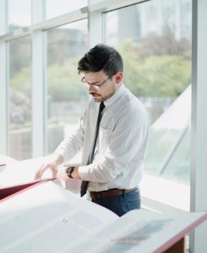 Regent College Library Services Manager Colton Whelpton turns the page of a volume of The Saint John's Bible Heritage Edition on display in the Regent Atrium.