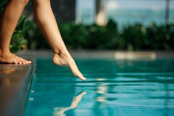 A girl's foot just about to touch the surface of a swimming pool.